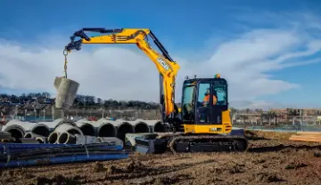  Ein Traktor mit Anhänger steht auf einem grünen Hügel, umgeben von saftigem Gras und klarem Himmel.
